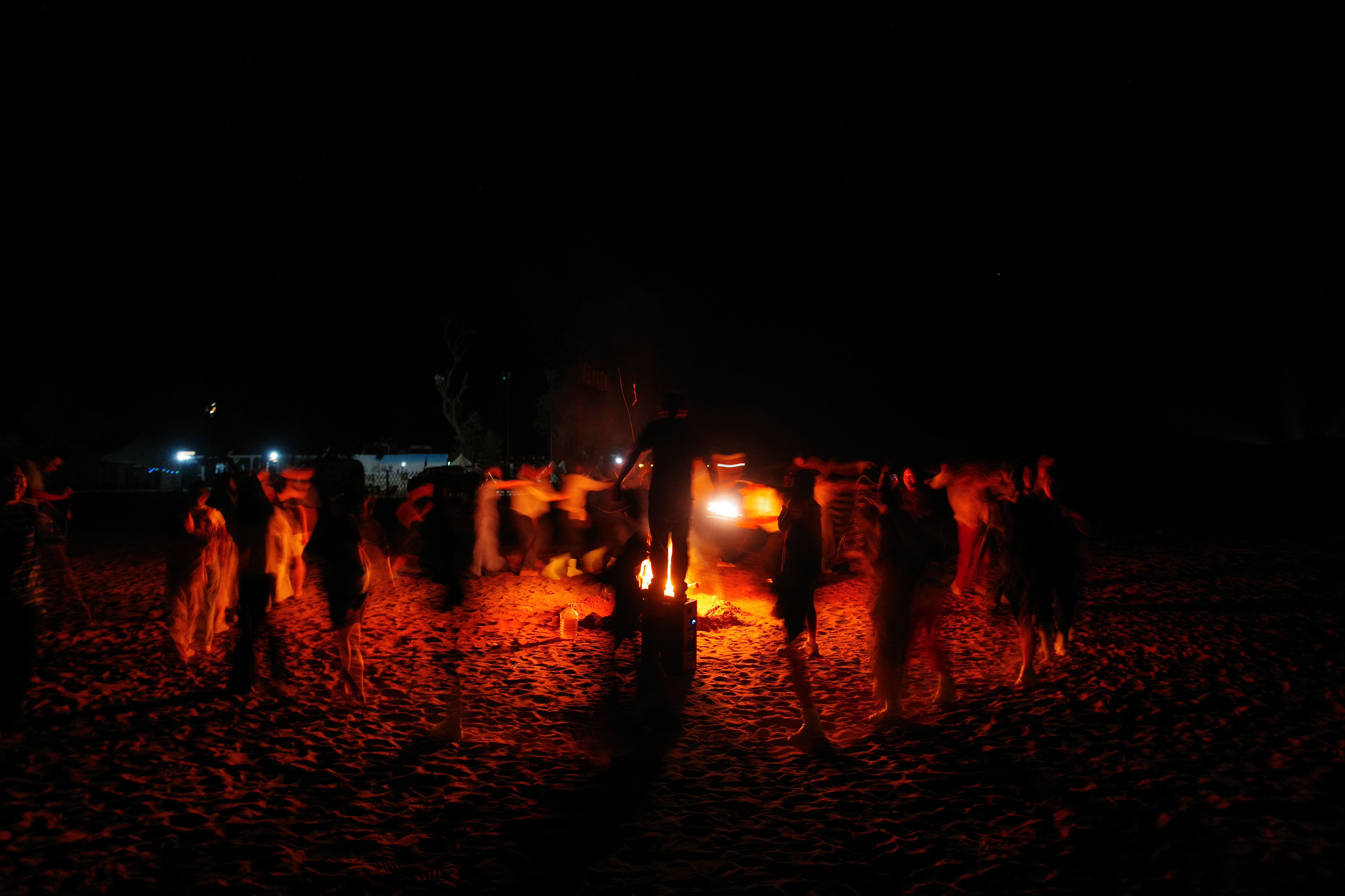 Blurred figures dancing around a desert bonfire at night, long exposure