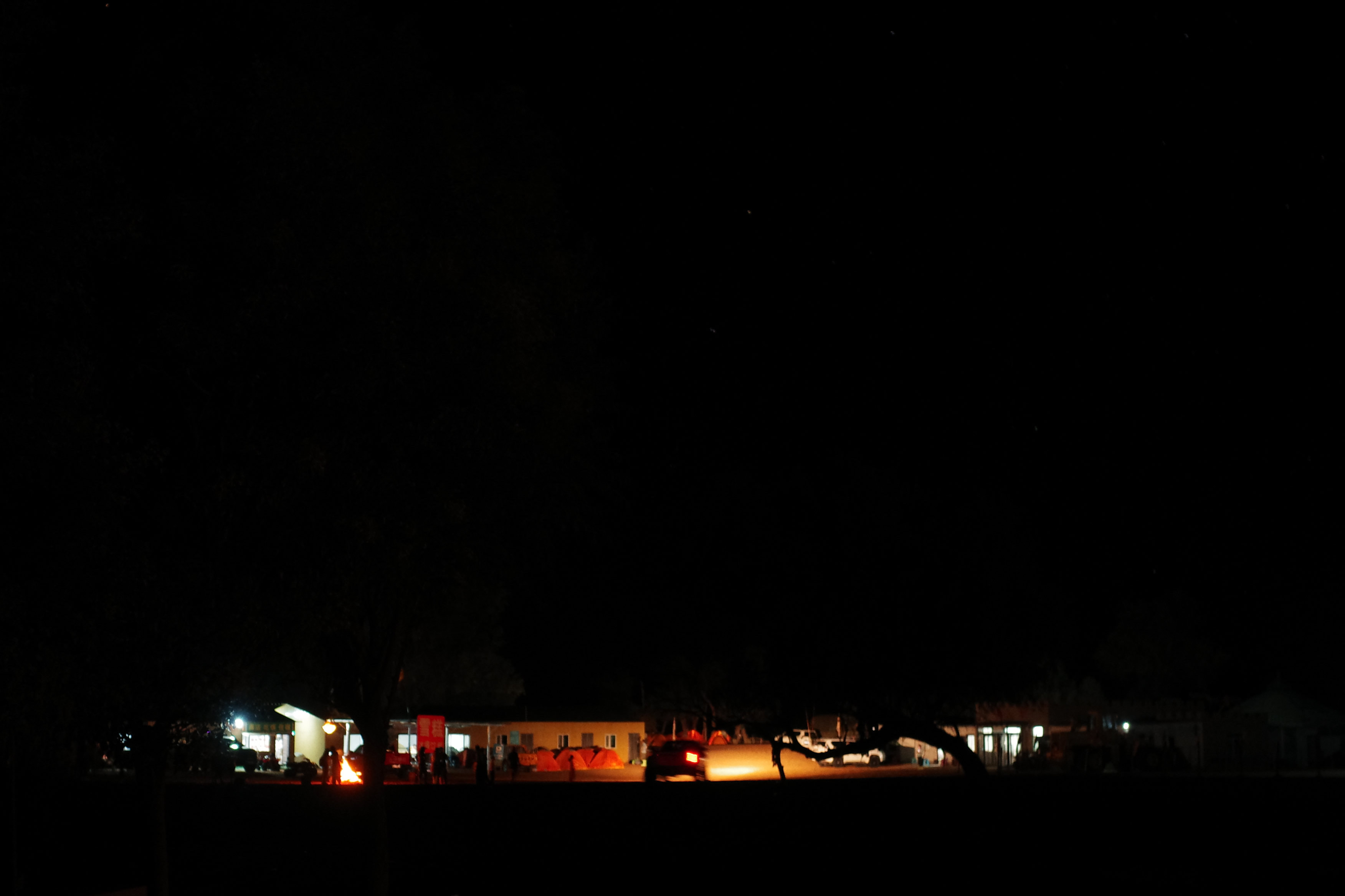 Distant night view of the lit campground buildings and a bonfire glowing under a dark sky