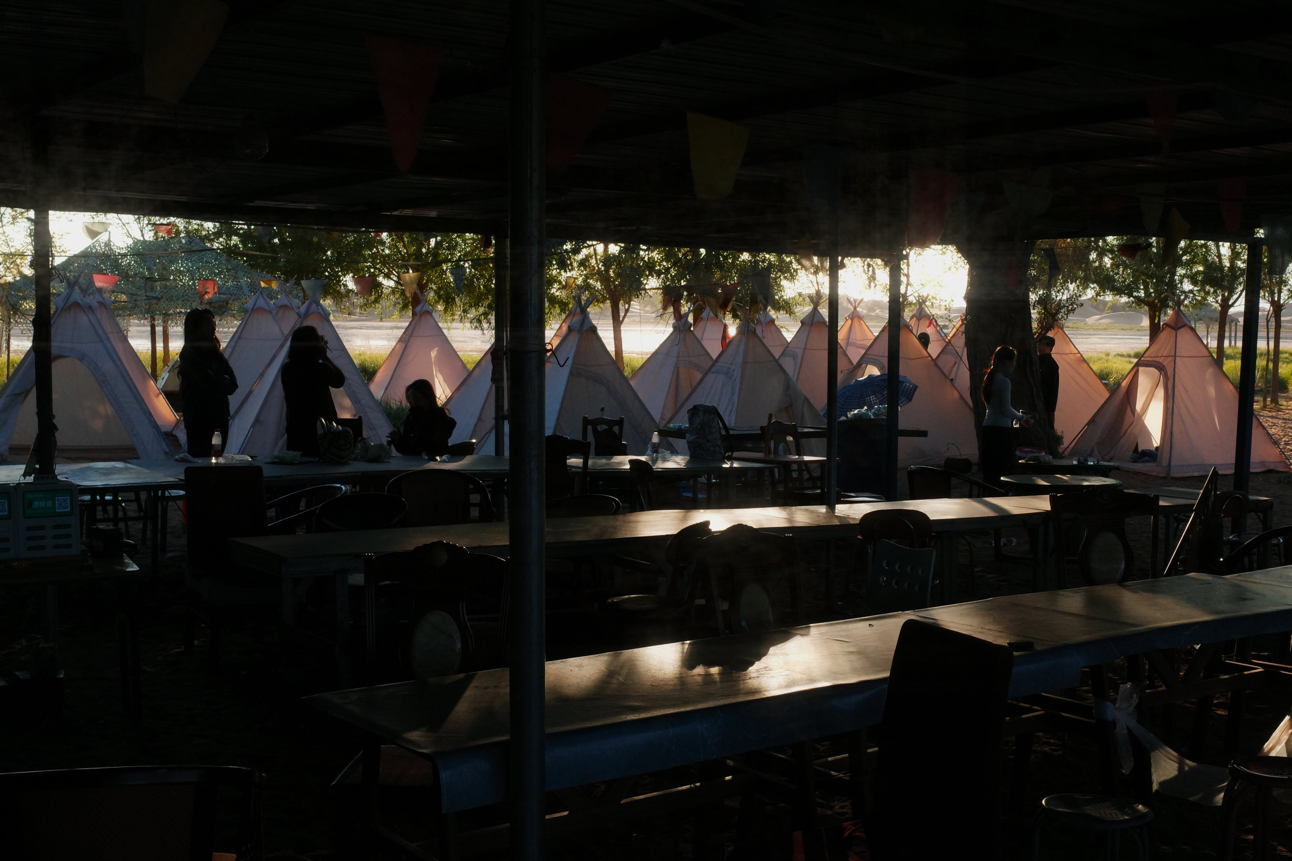 Morning light through an open-air shelter looking out at a row of teepee tents
