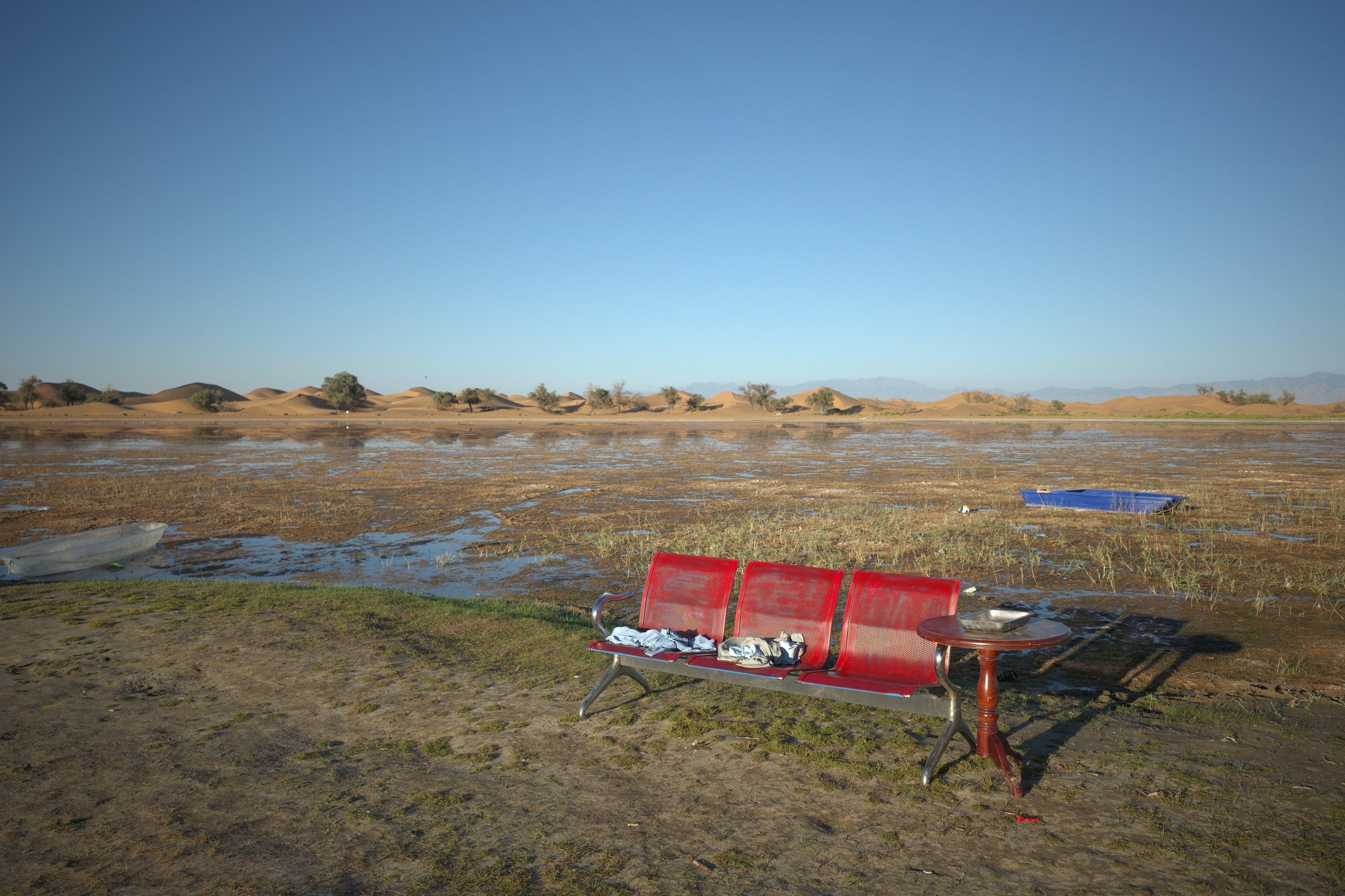 A row of red bench seats and small boats on a flooded oasis shoreline at dusk