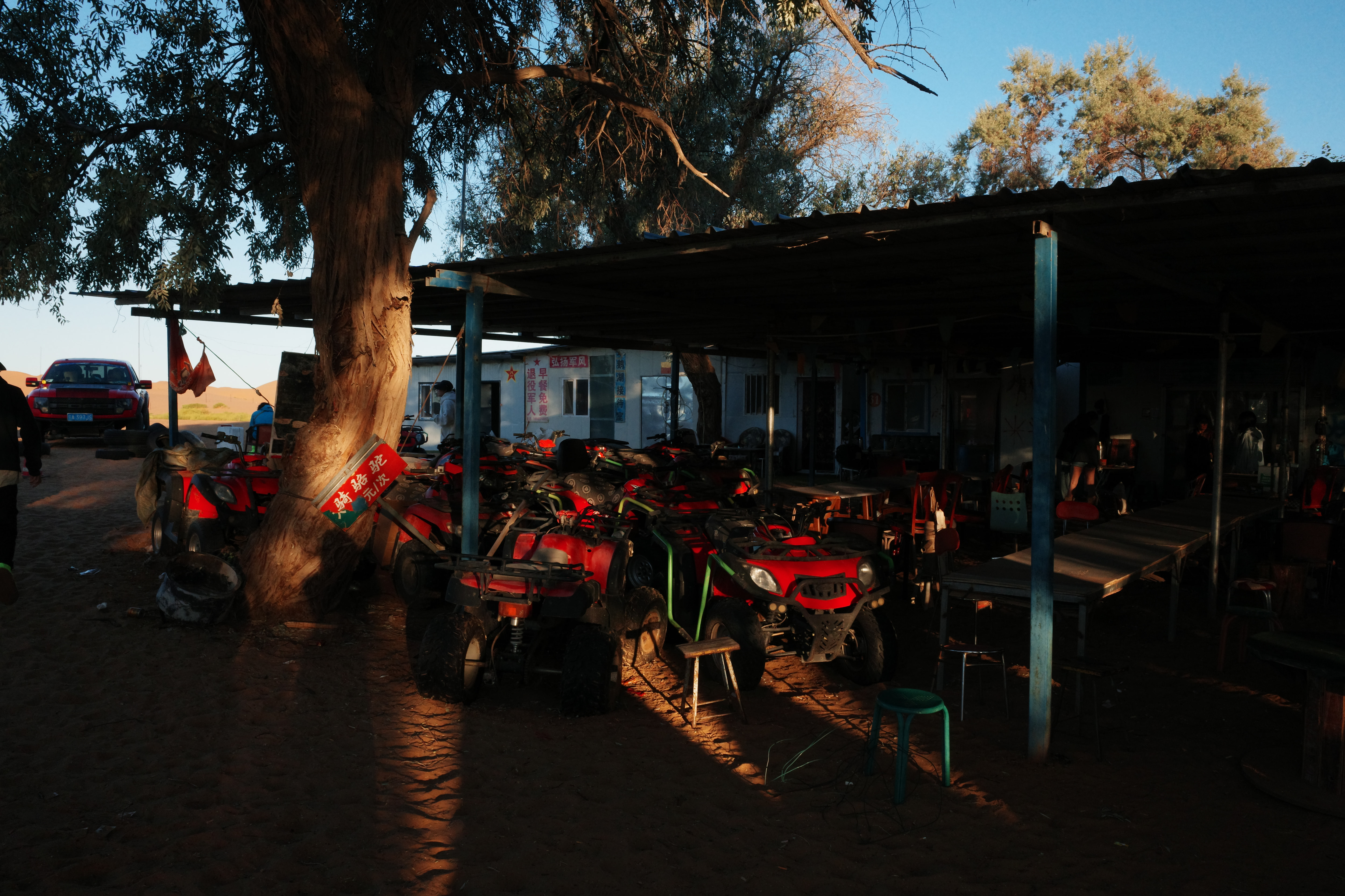 Red pickup truck and quad bikes parked under a tree-shaded shelter in morning light