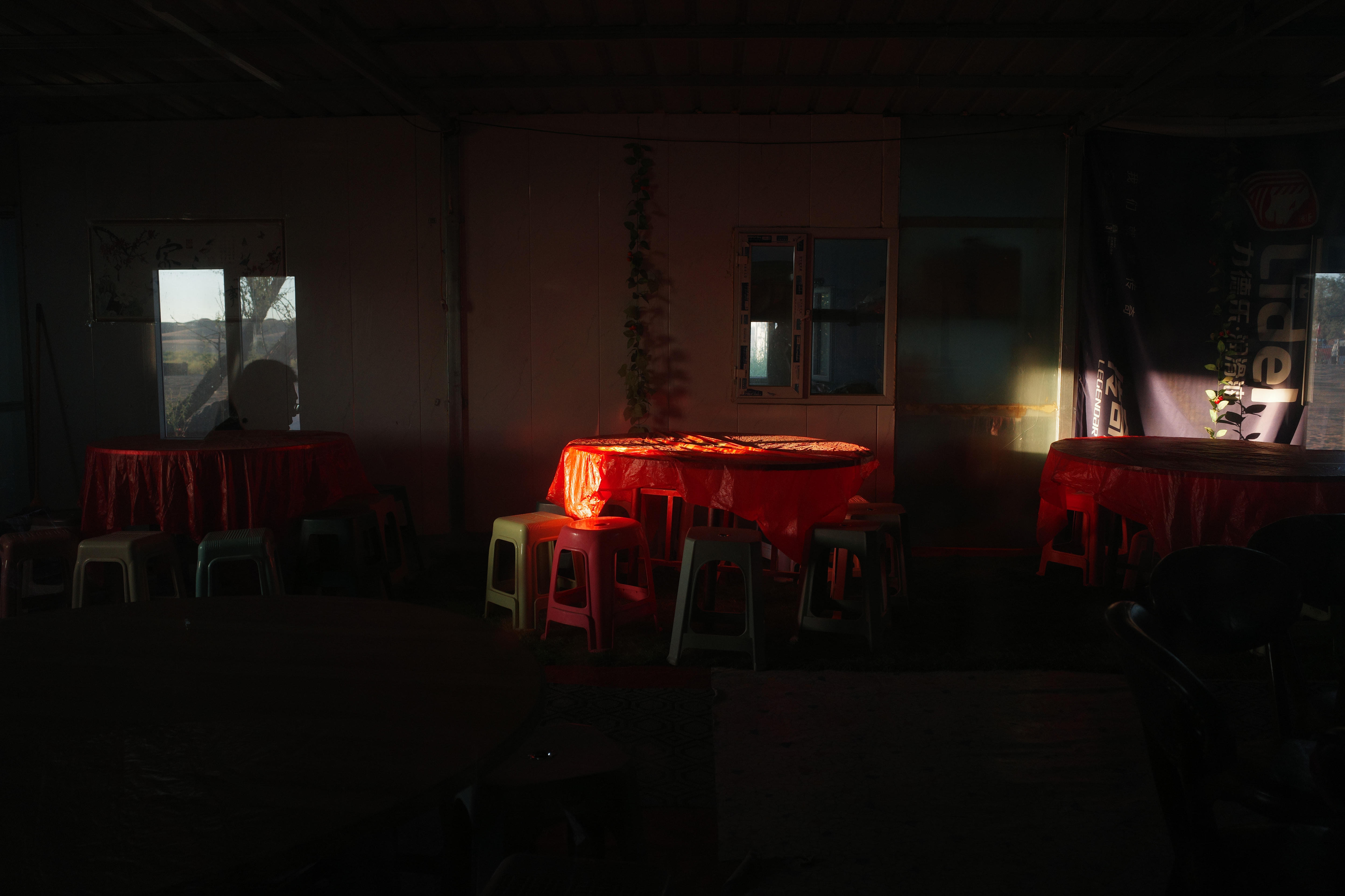 Dim dining room with red tablecloths lit by low evening sun through the windows