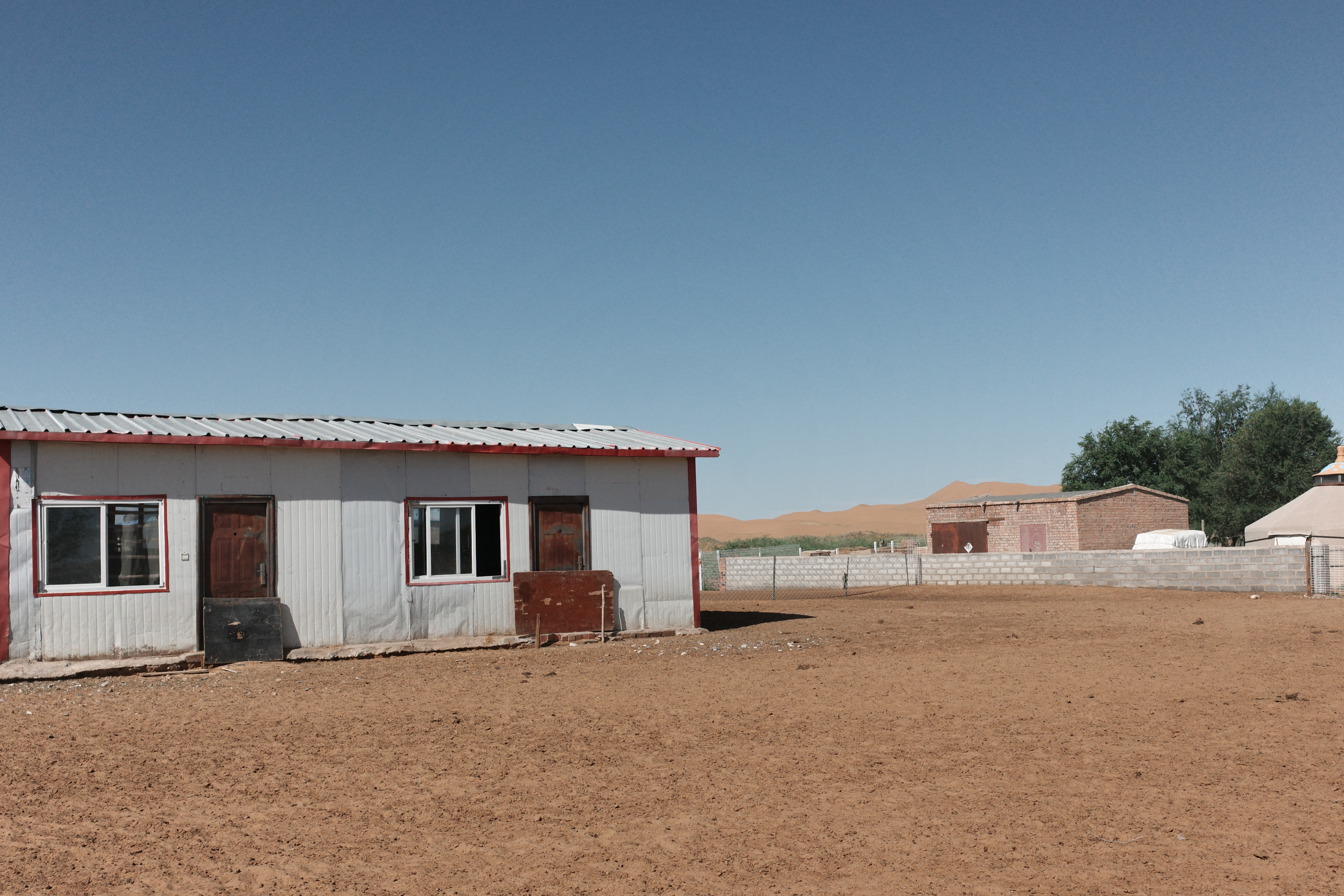A corrugated-metal building with red trim, a brick building and a yurt visible beyond it